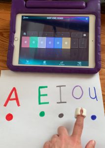 Finger with specdrums tapping colored dots below vowels